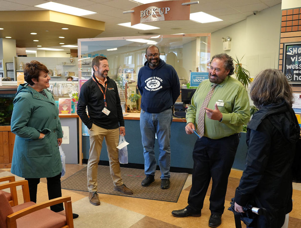 Group of people standing and talking inside pharmacy waiting area.